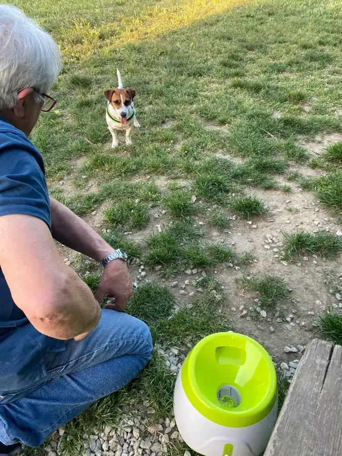 A man crouching in a garden with his jack russell and the launcher